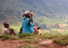 Elderly woman making a peace sign sitting by a dirt road with children