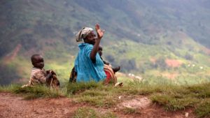 Elderly woman making a peace sign sitting by a dirt road with children